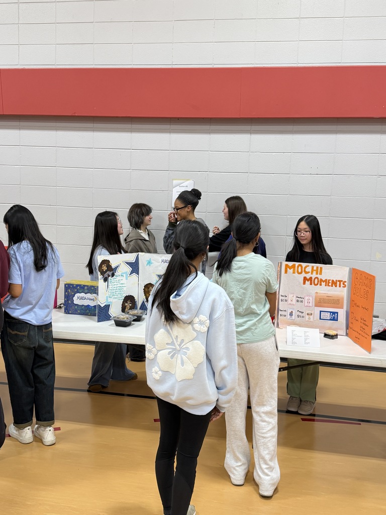 Students standing at a table of projects.
