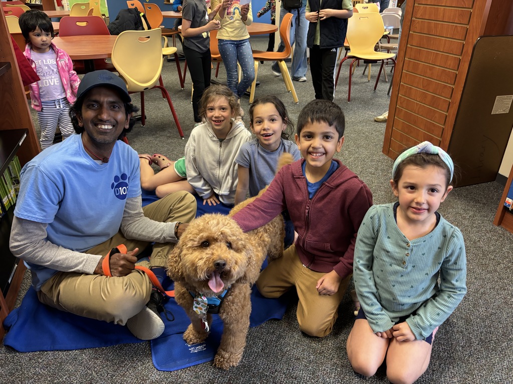 Students petting a dog with the dog owner.