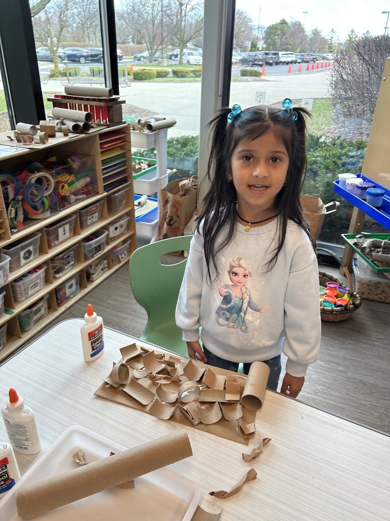Girl standing at a table with art supplies, smiling.