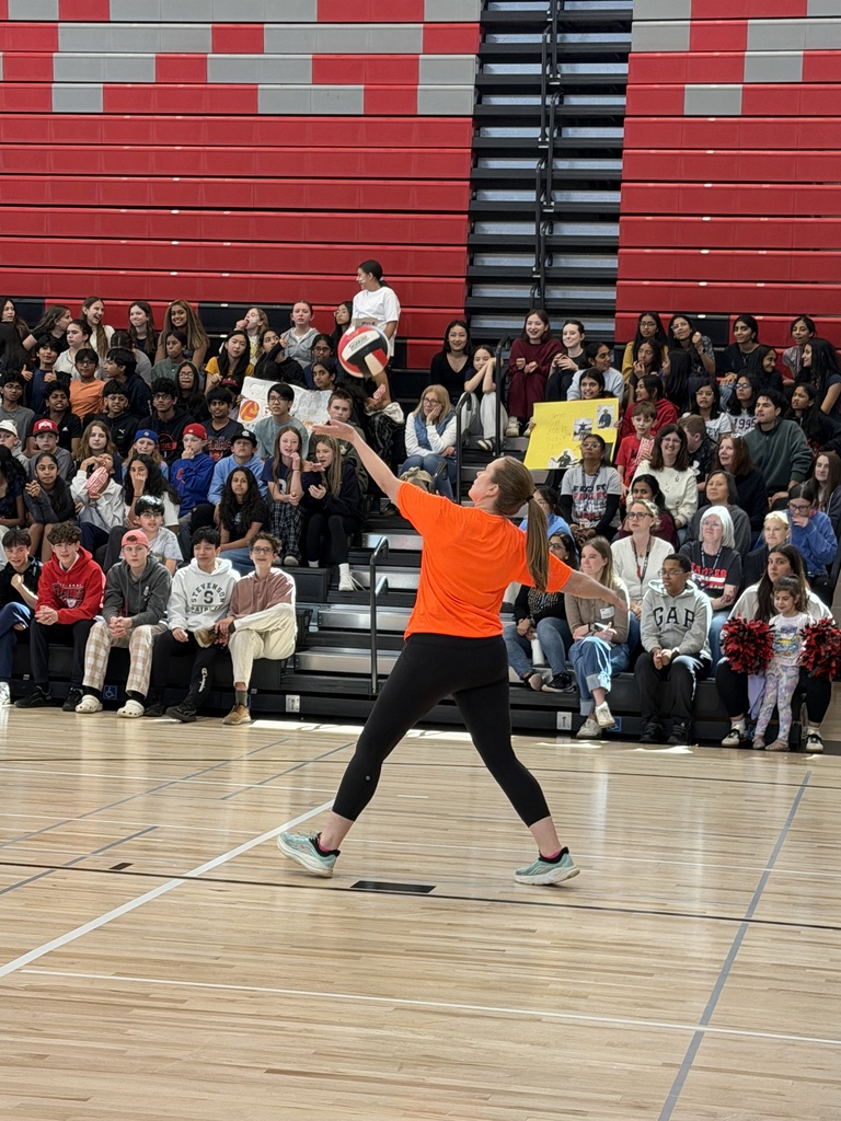 Dr. McIntyre serving the ball with kids in the background in the stands.