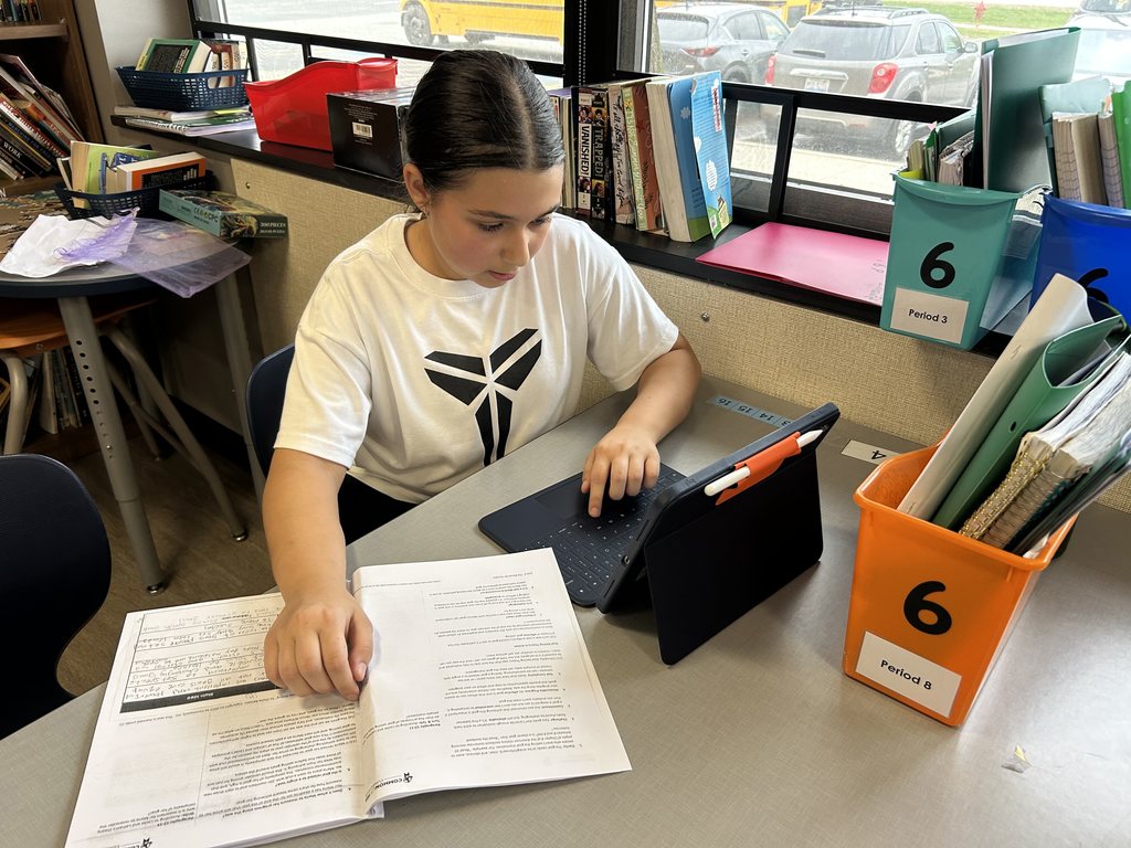 Student working on her ipad with a book in front of her, too.