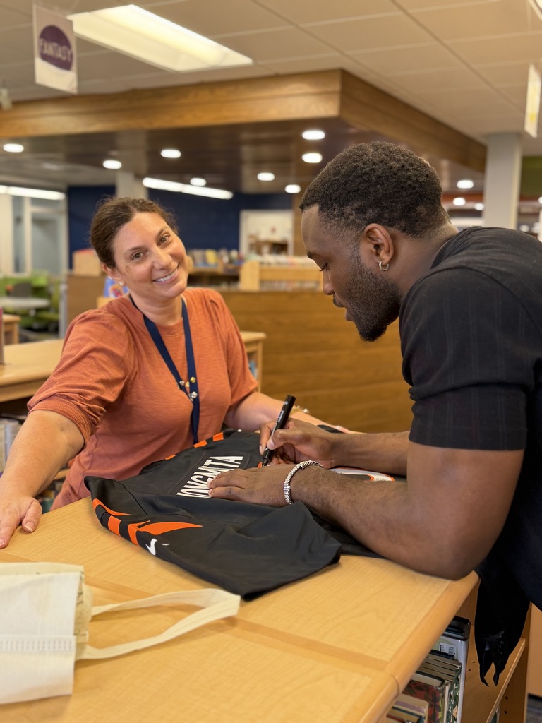 Mrs. Tamez smiling while Njongmeta signs a jersey.