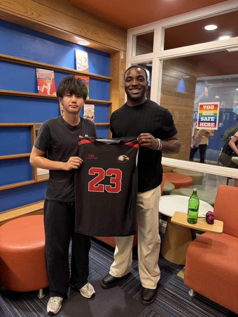 Njongmeta standing with a student, holding his AJHS jersey.