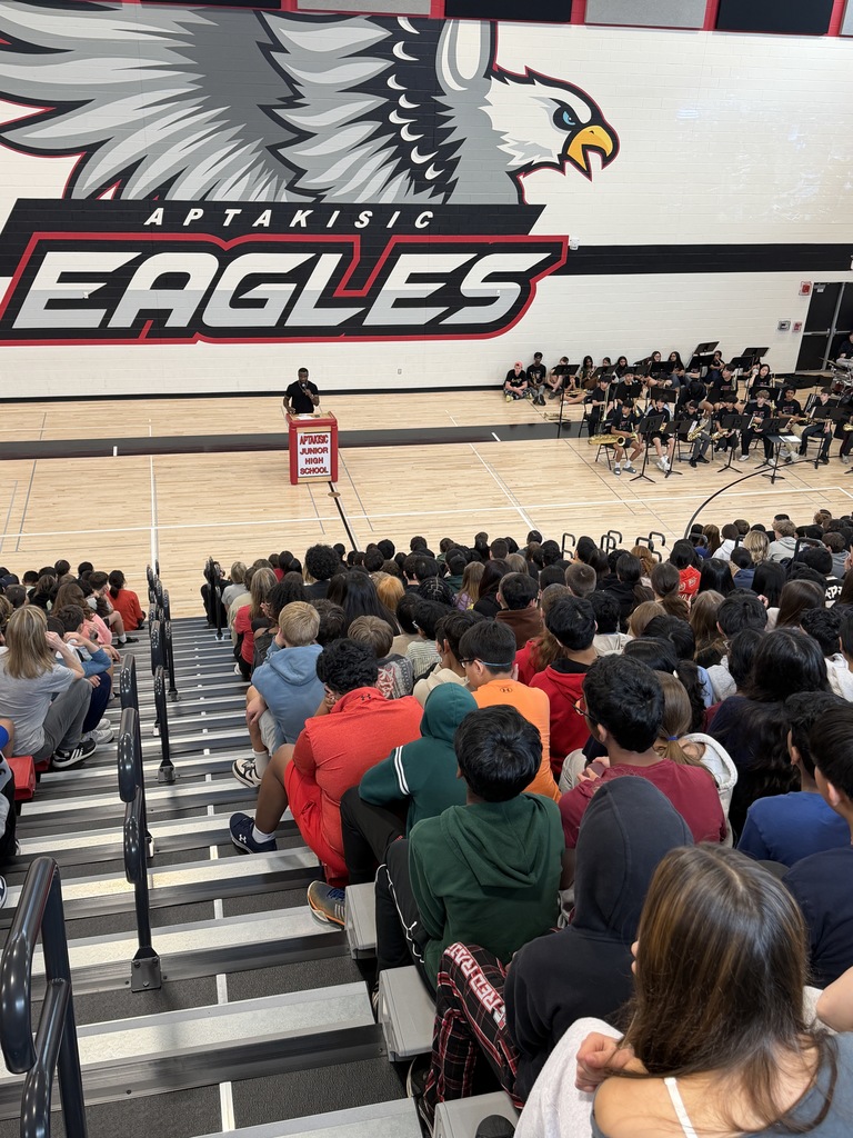 Njongmeta standing and speaking at a podium with students in front of him in bleachers.