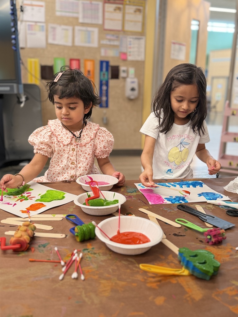 2 girls standing and painting at a table.