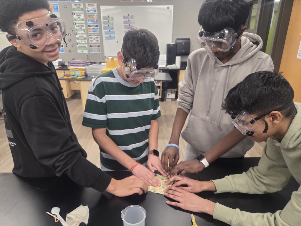 4 boys working on a science project at a black table.