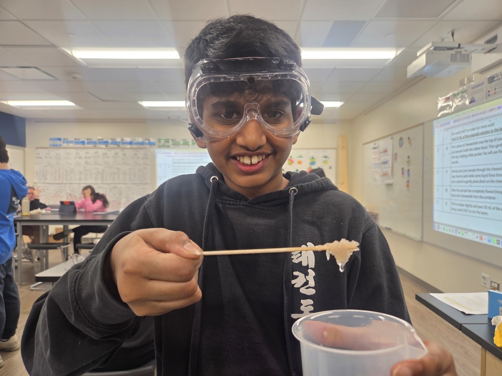 Boy holding the goo on a stick. Wearing goggles and smiling. 