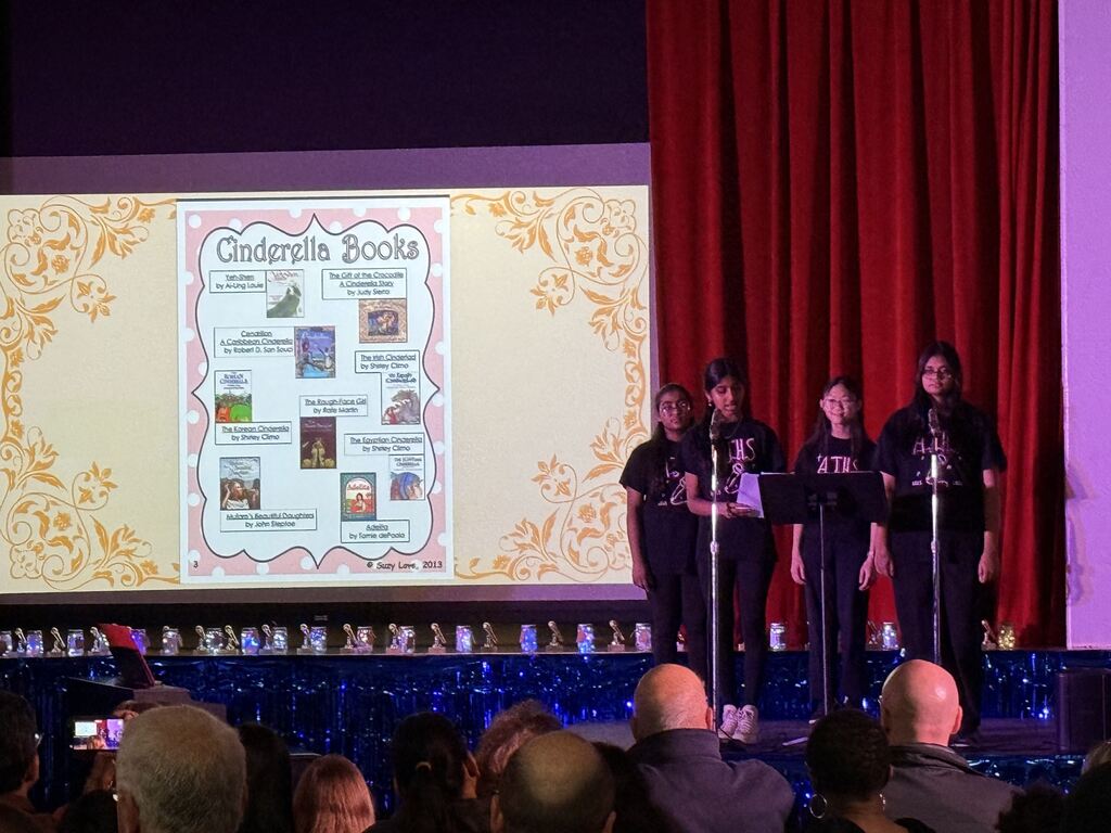 Students speaking into a microphone on stage.