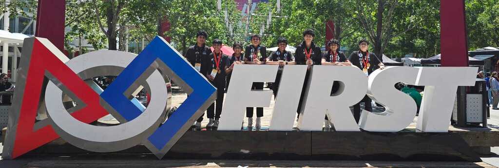 Robotics team poses by large sign outside that says "FIRST"