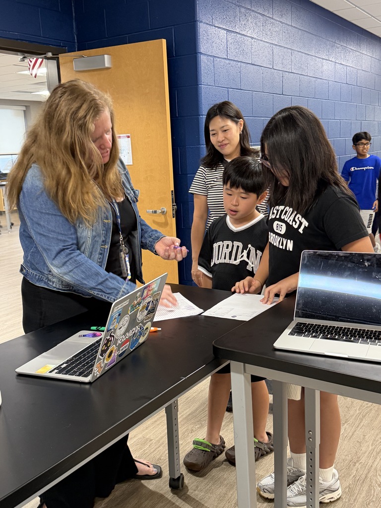 family talking to a teacher standing at a desk.