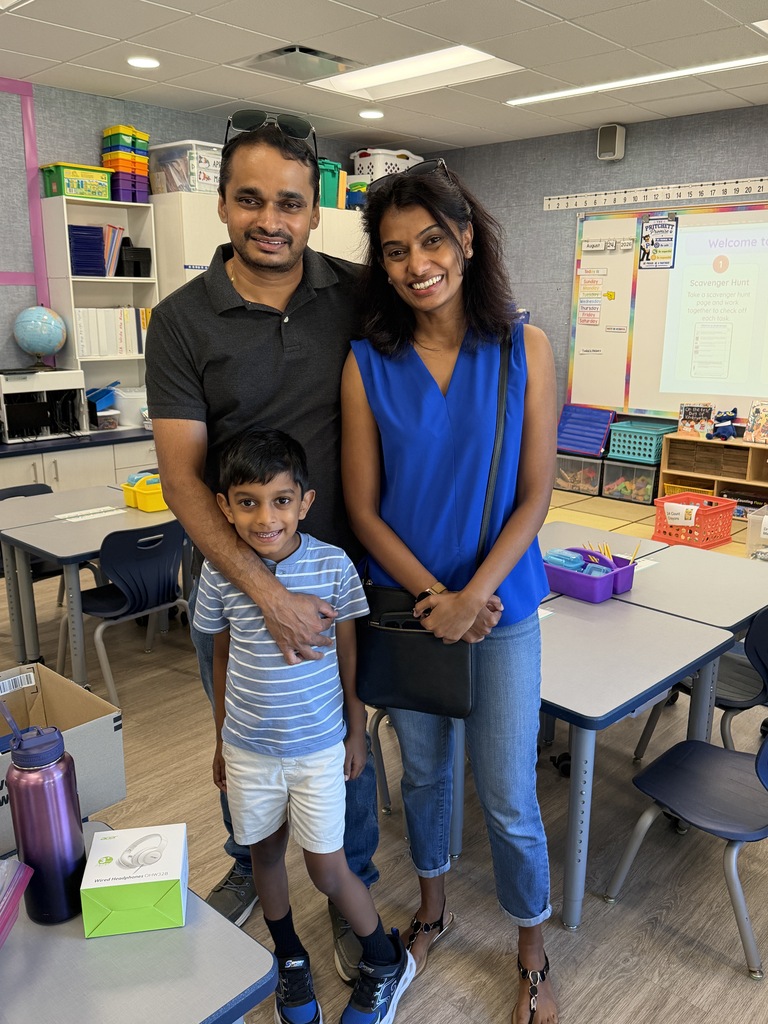 STudent standing with his parent in a classroom.