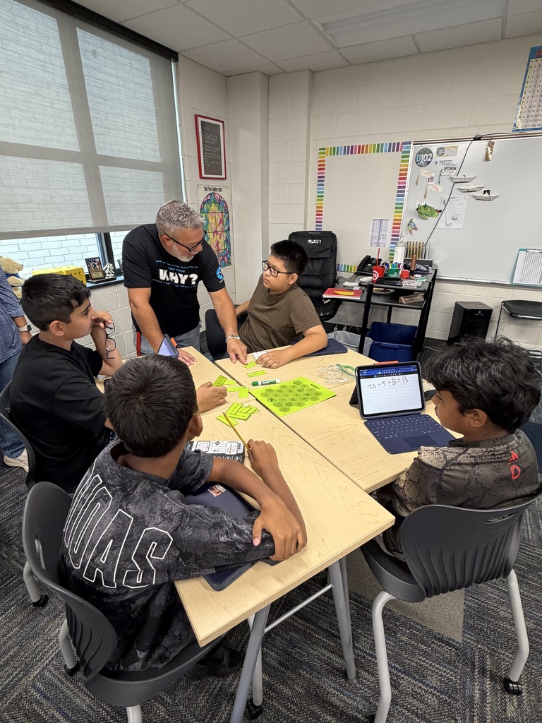 Teacher leaning over a table helping 4 boys on the math game.
