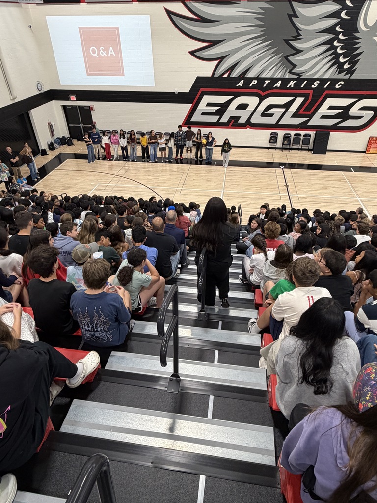STudents sitting in the bleachers watching a presentation in the gym.