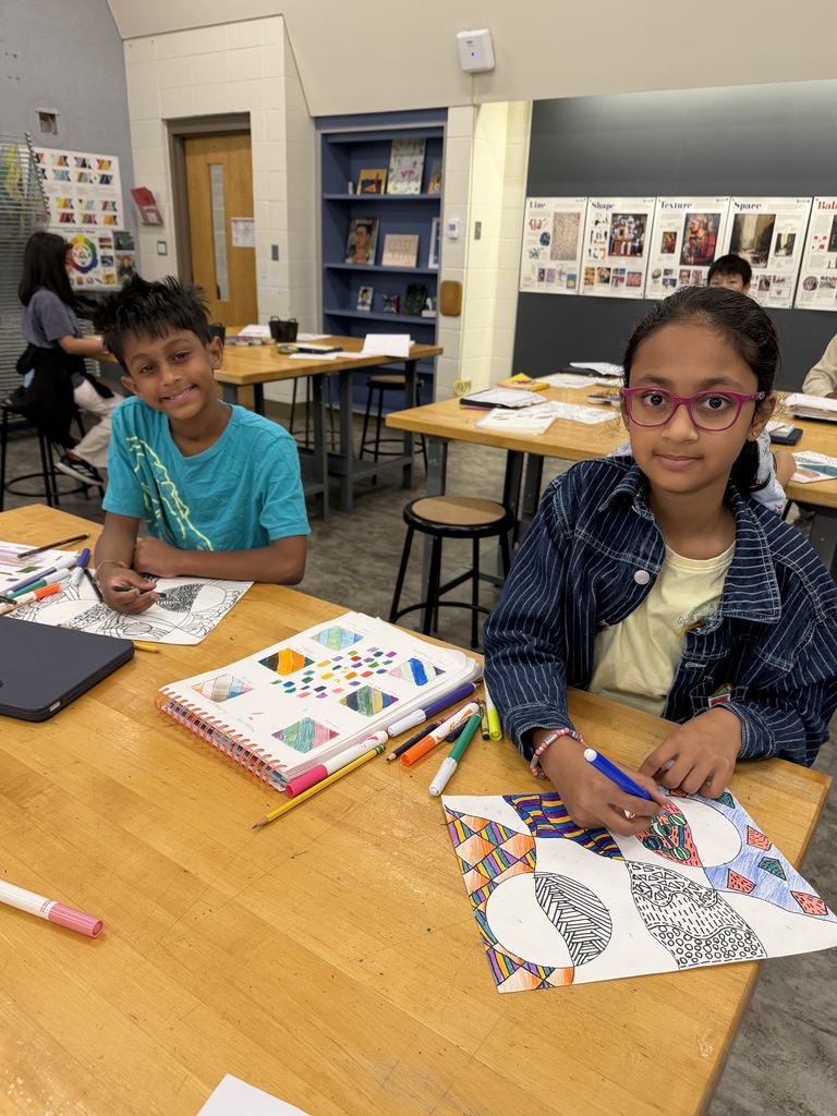 2 students sitting at a table with their artwork.