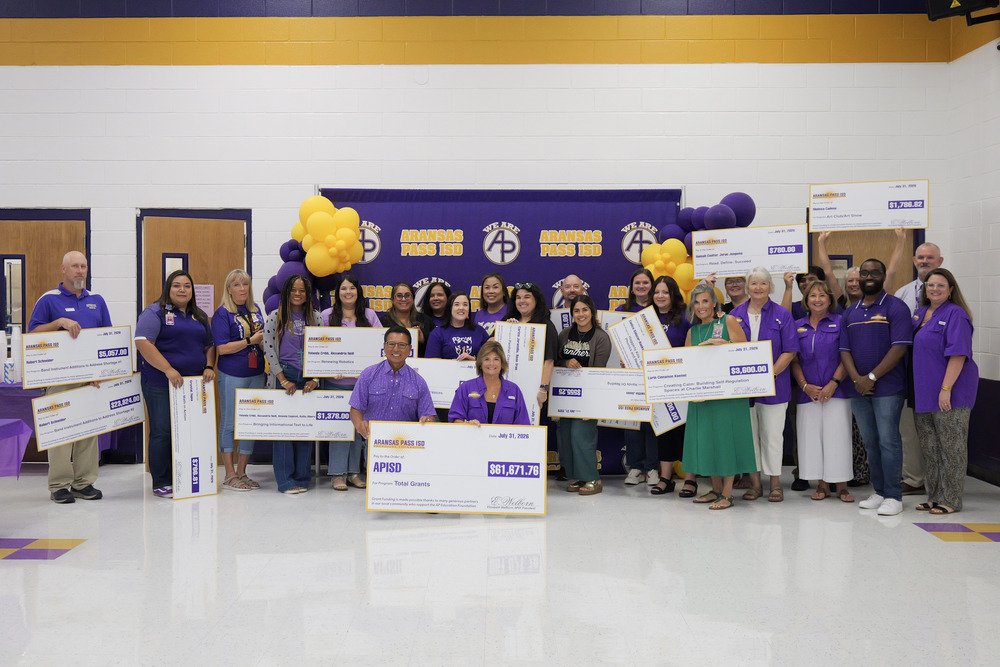 group of teachers holding large ceremonial checks in front of a purple backdrop