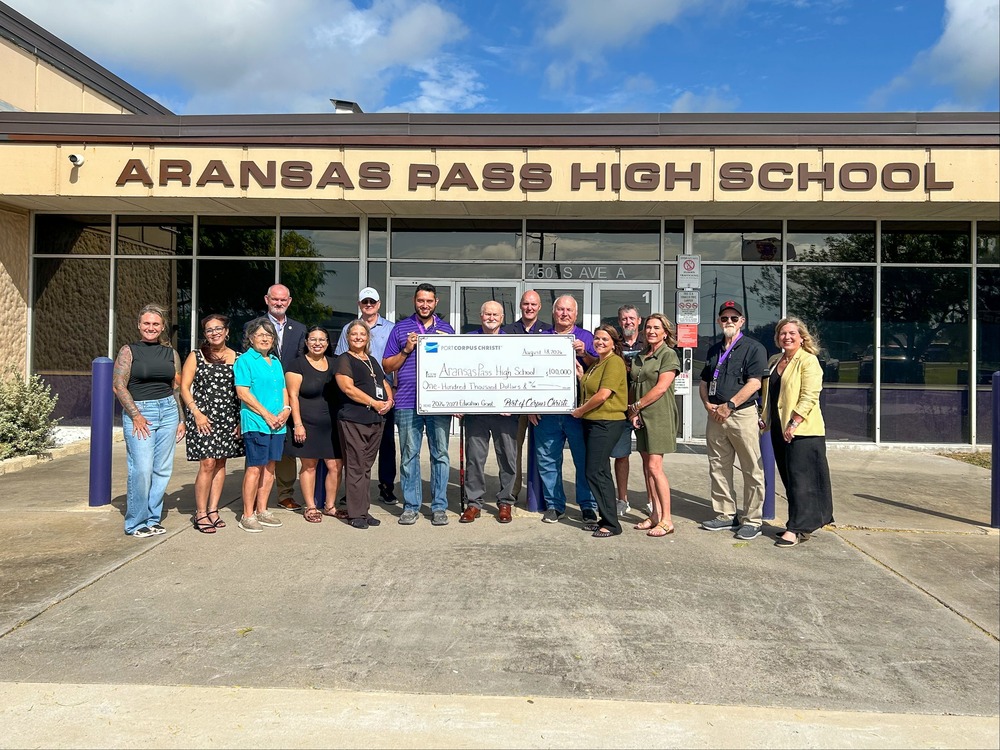 group of people standing in front of a building that says "Aransas Pass High school" holding a ceremonial check.