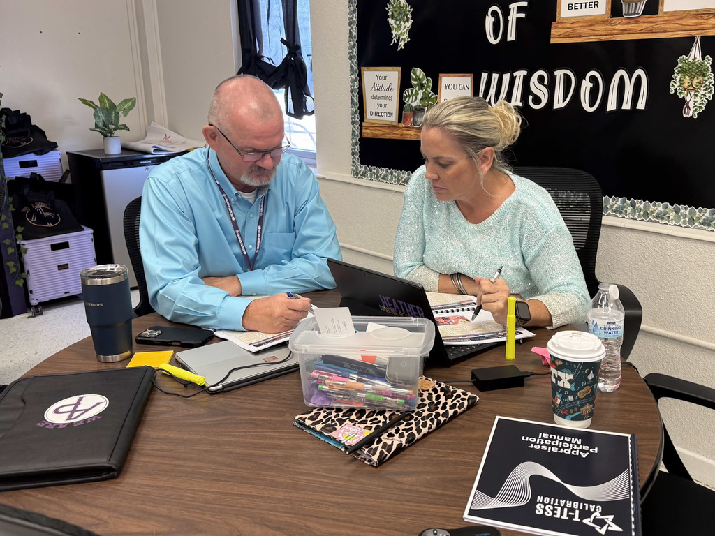 Two adults sitting at a table completing training with notebooks and laptop