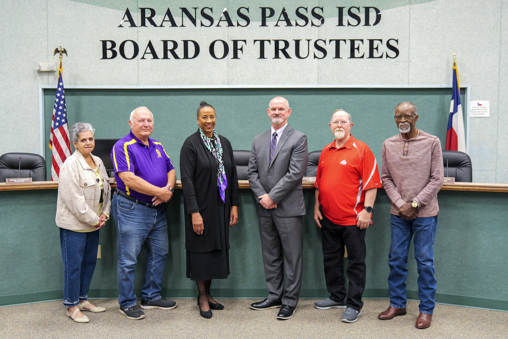 Six people standing in front of wording on a wall that says Aransas Pass ISD Board of Trustees