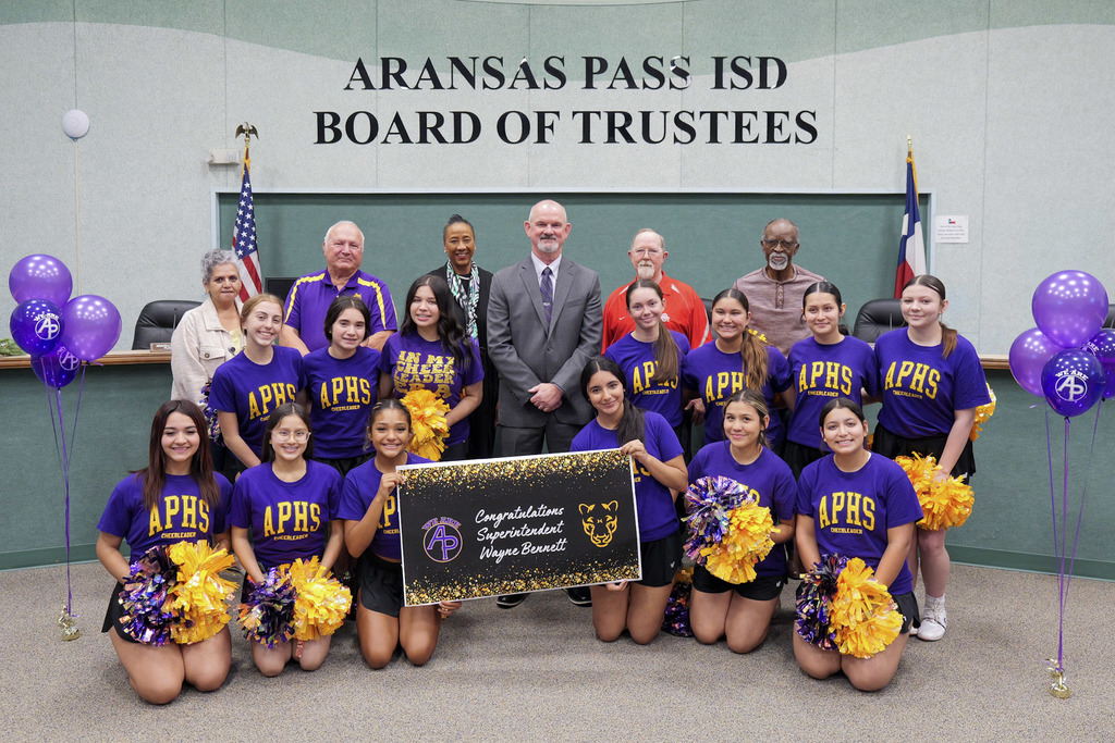 Large group standing in a boardroom holding a sign that says Congratulations Superintendent Wayne Bennet