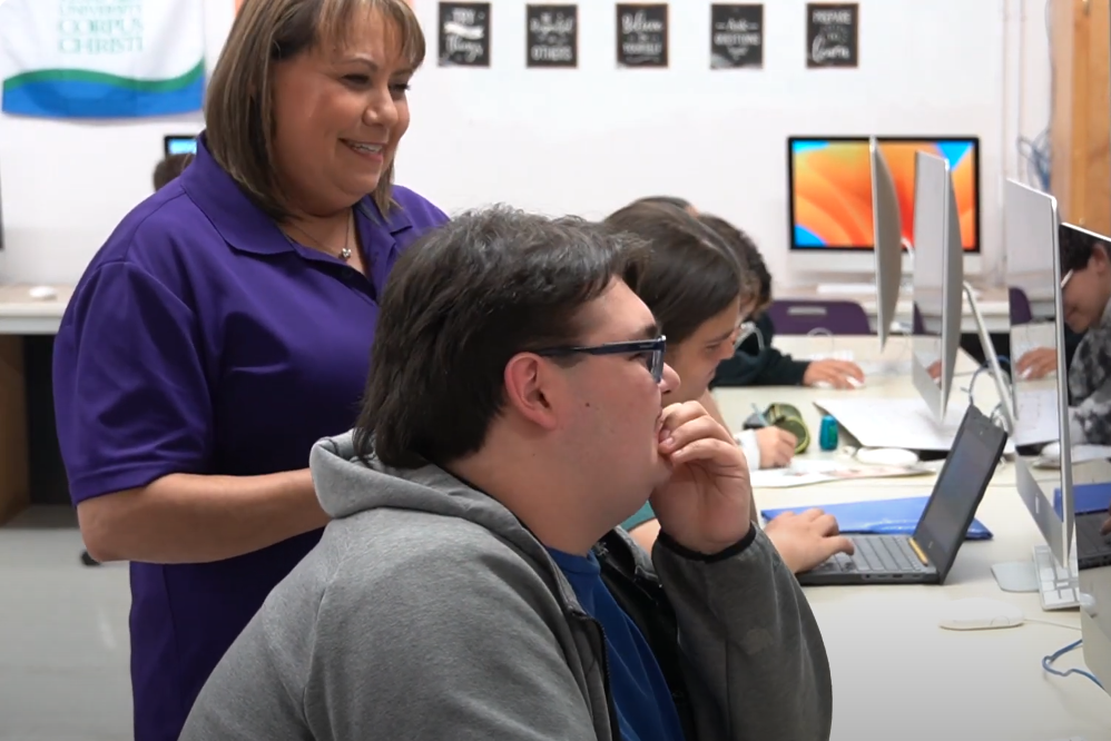 teacher standing next to students working on computers