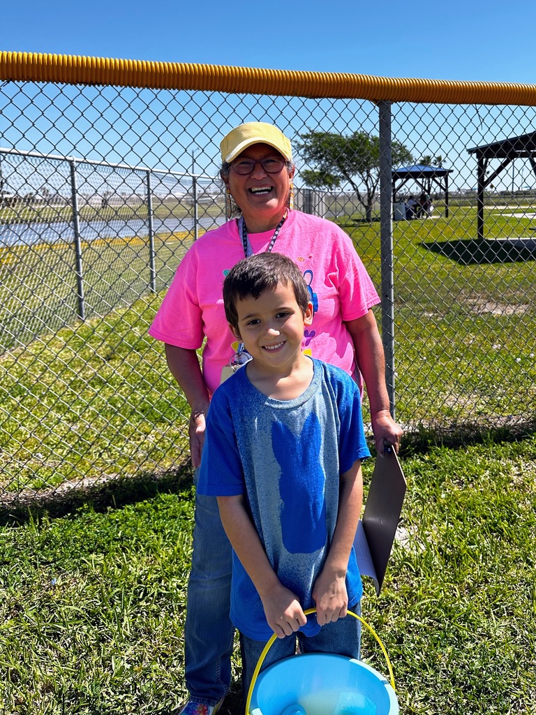 student and teacher standing in a grassy park in front of a fence.