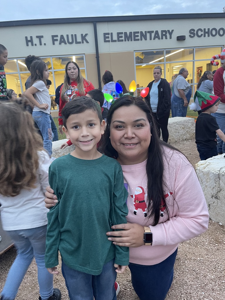 Student standing next to teacher kneeling in front of a school.