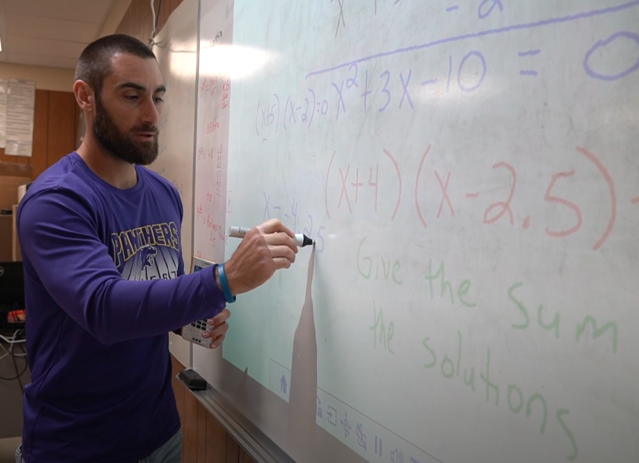teacher writing math problem on a white board