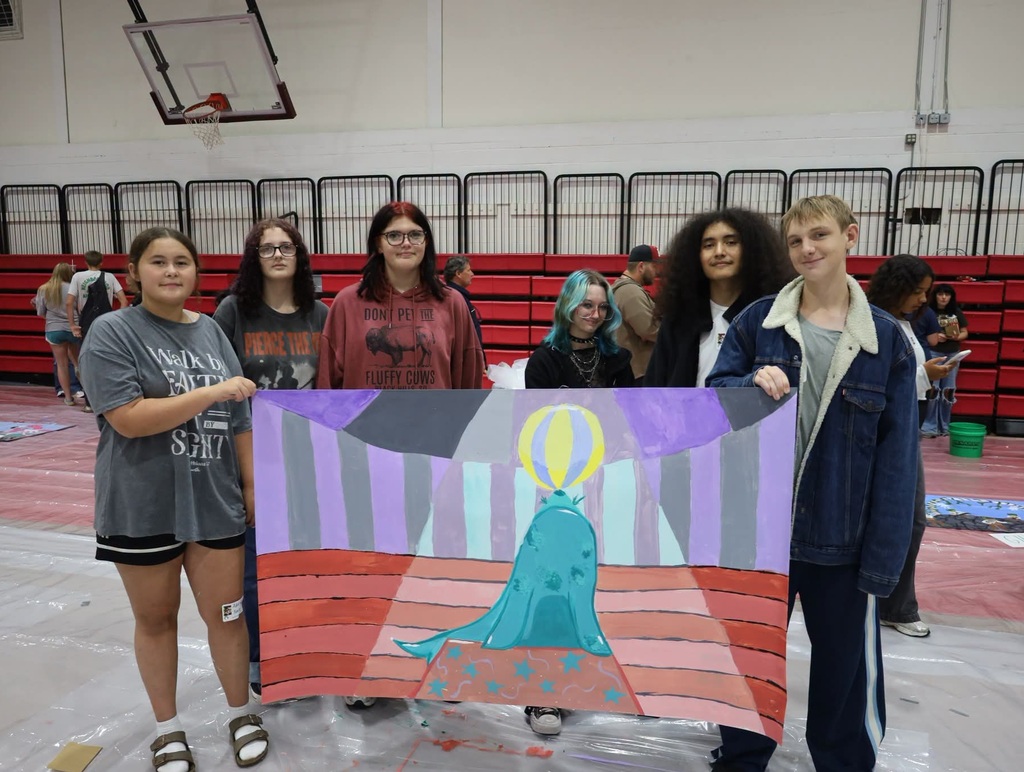 All six students holding up the finished mural. The white cone has been filled in with lighter versions of the other colors to imply light. The podium has been covered with teal stars. A yellow and gray ball is perched on the seal's nose.