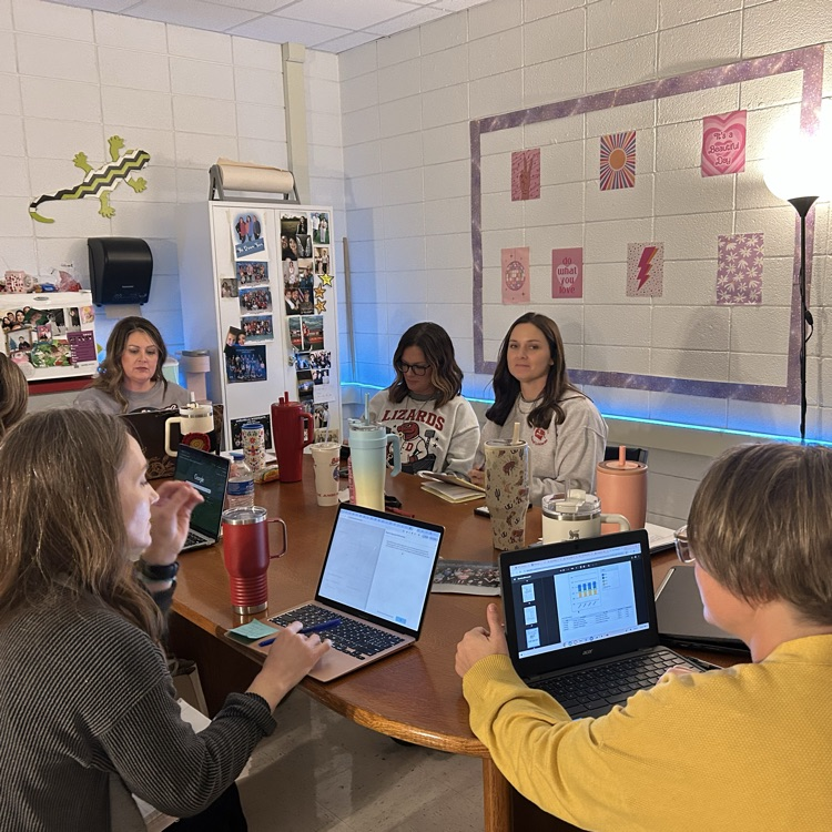 Group of teachers around a table with laptops discussing most recent interim data  