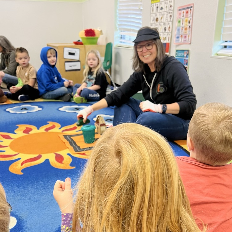 professional educator sitting in front of children on carpet. Telling a story with props.