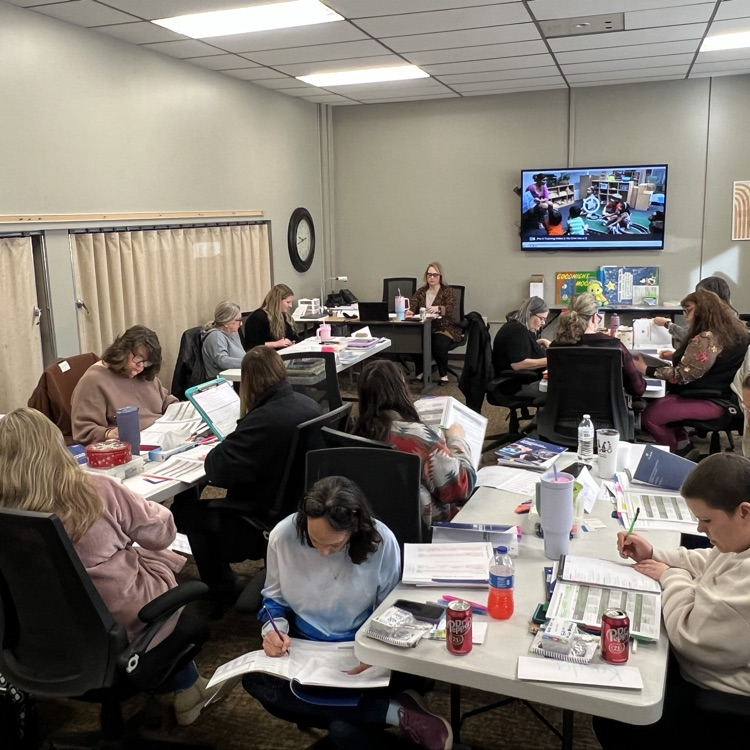 professional educators, seated at tables watching a preschool classroom via video practicing the coding process for class observations.