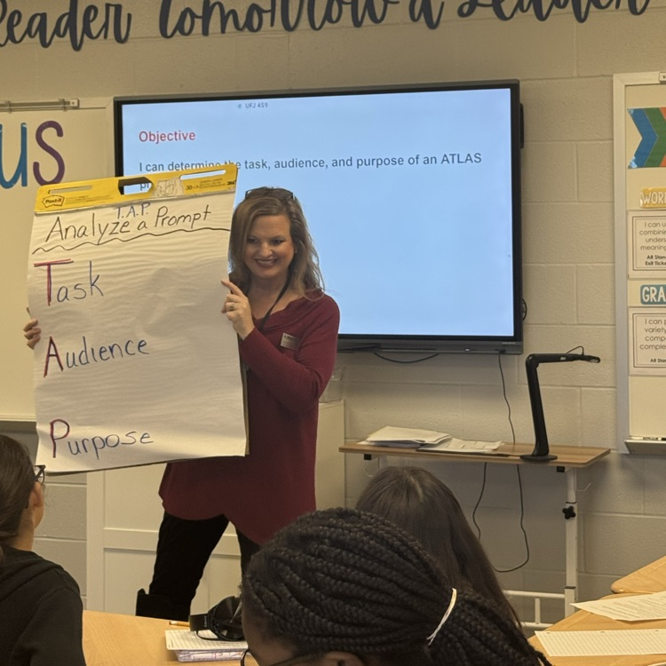 Teacher holding chart at the front of the room with his to break down a writing prompt  