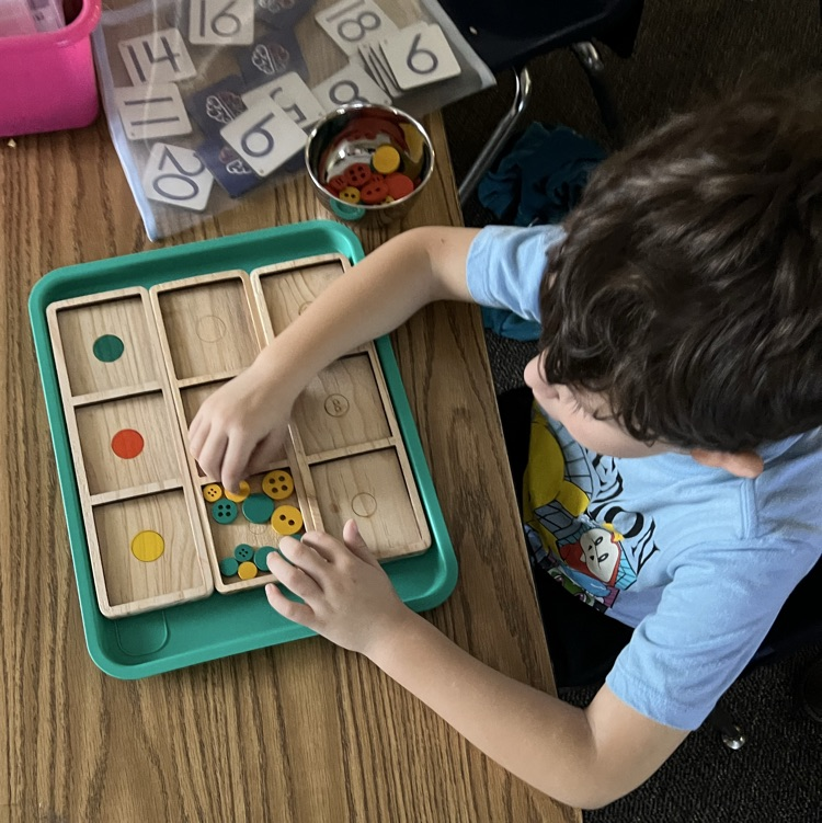 Child sitting at a table working on a feeling brains tray that is a math activity with numbers and buttons