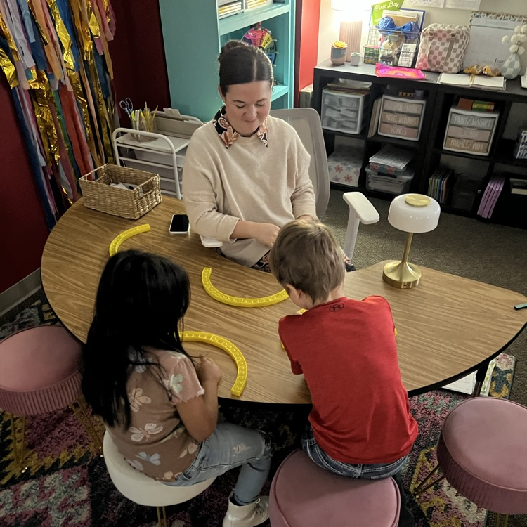 professional educator sitting at a table working in a small group with two children
