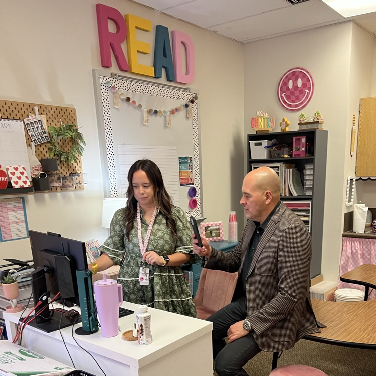 teacher standing, showing another educator something on a computer screen