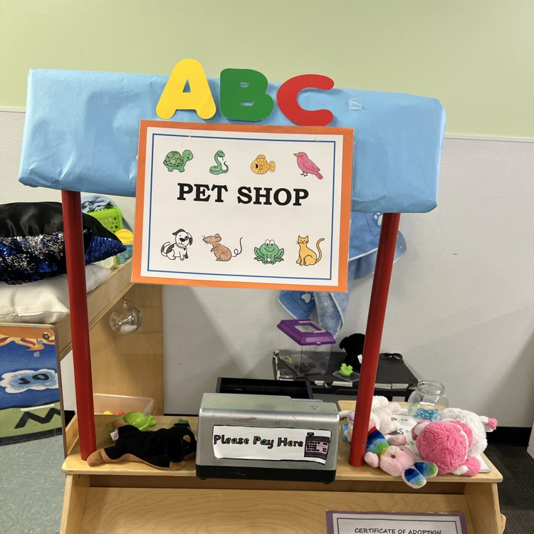 Dramatic play center labeled “ABC Pet Shop” with stuffed animals, a toy cash register, and adoption certificates set up for imaginative play.