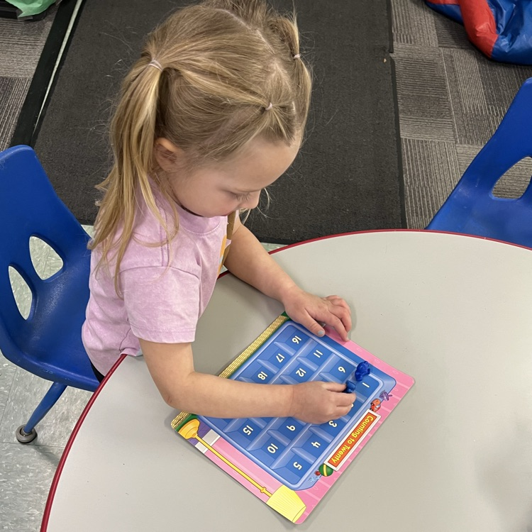 Young child working independently at a table using a counting board with numbered squares and small manipulatives for early math practice.