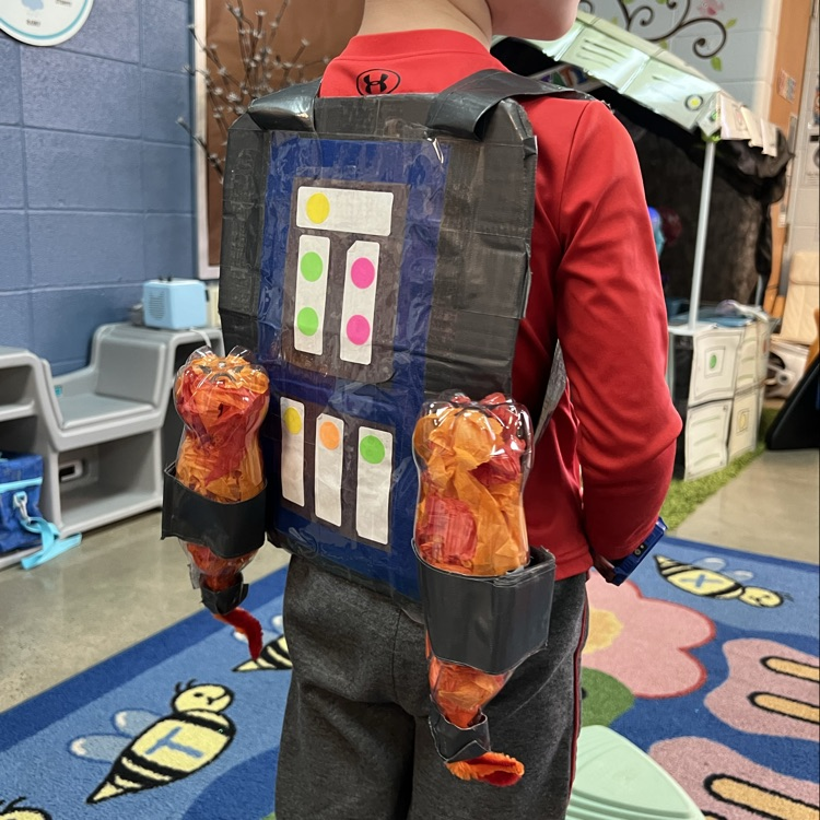 Preschool student wearing a handmade cardboard jetpack during a space-themed learning activity in the classroom.