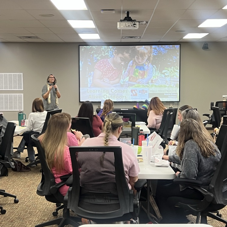 Early childhood educators sit at tables during a professional learning session about outdoor learning.