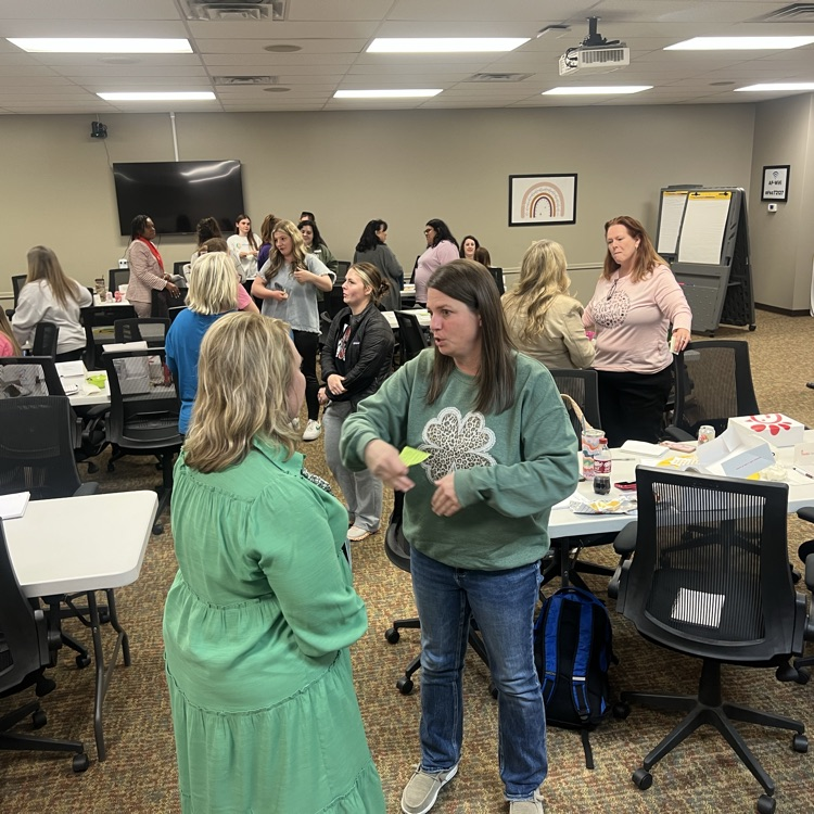 Early childhood providers stand and talk in small groups during a collaborative learning activity.