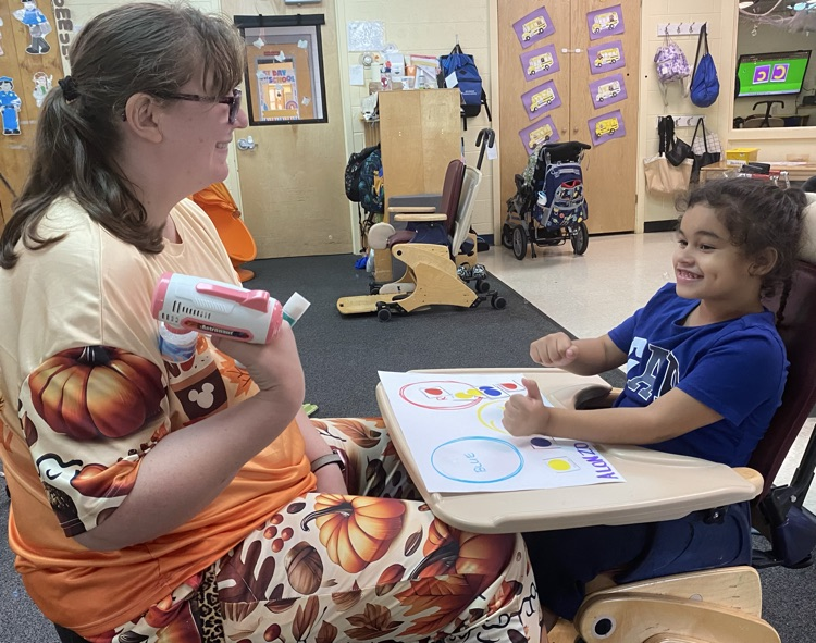 Student and staff member smiling and having fun with bubble machine.