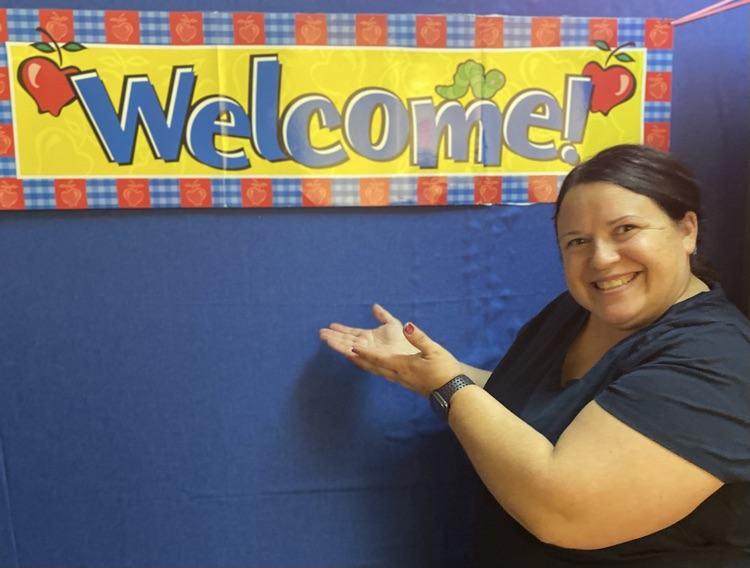 ADS Teacher smiling in front of classroom Welcome sign.