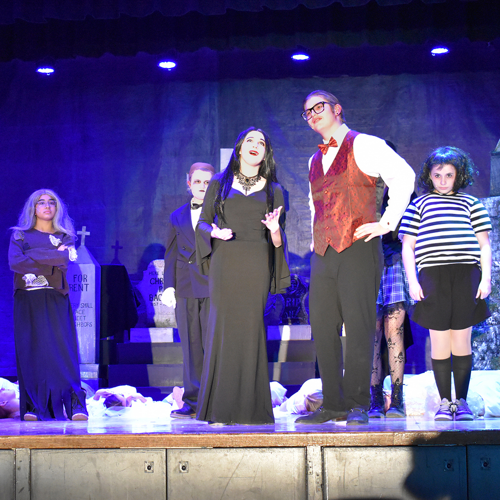 Scene from the LMS performance of The Addams Family Musical, with Morticia and Gomez Addams center stage