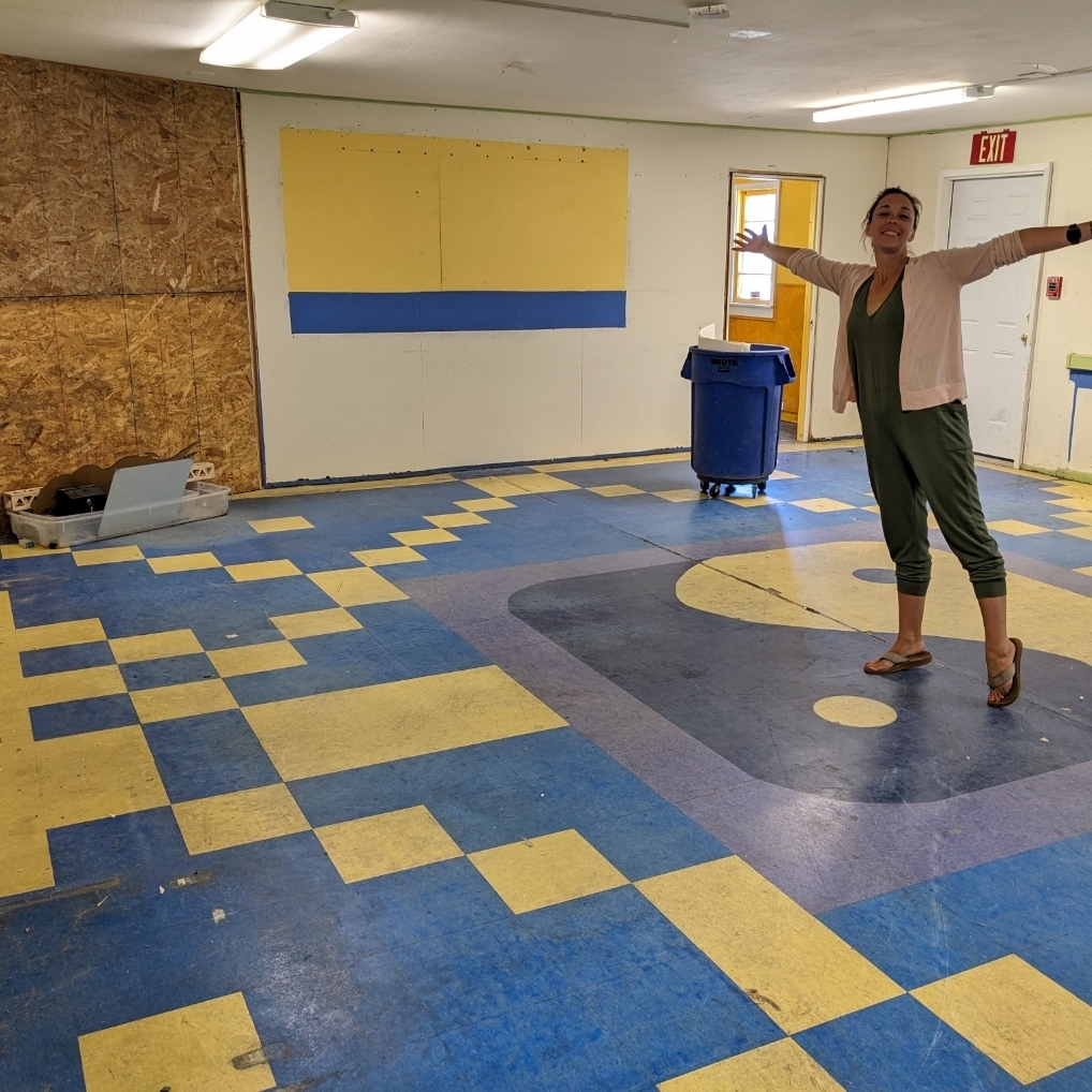 Inside empty science room with adult posed with arms outstretched.