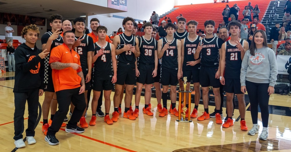 A high school boys' basketball team in black and orange uniforms and orange shoes poses for a photo with a second-place trophy.