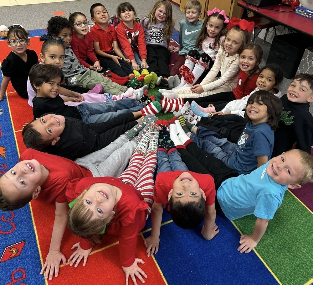 A group of children sit in a circle with their feet pointed toward the middle. They wear brightly colored holiday-themed socks.