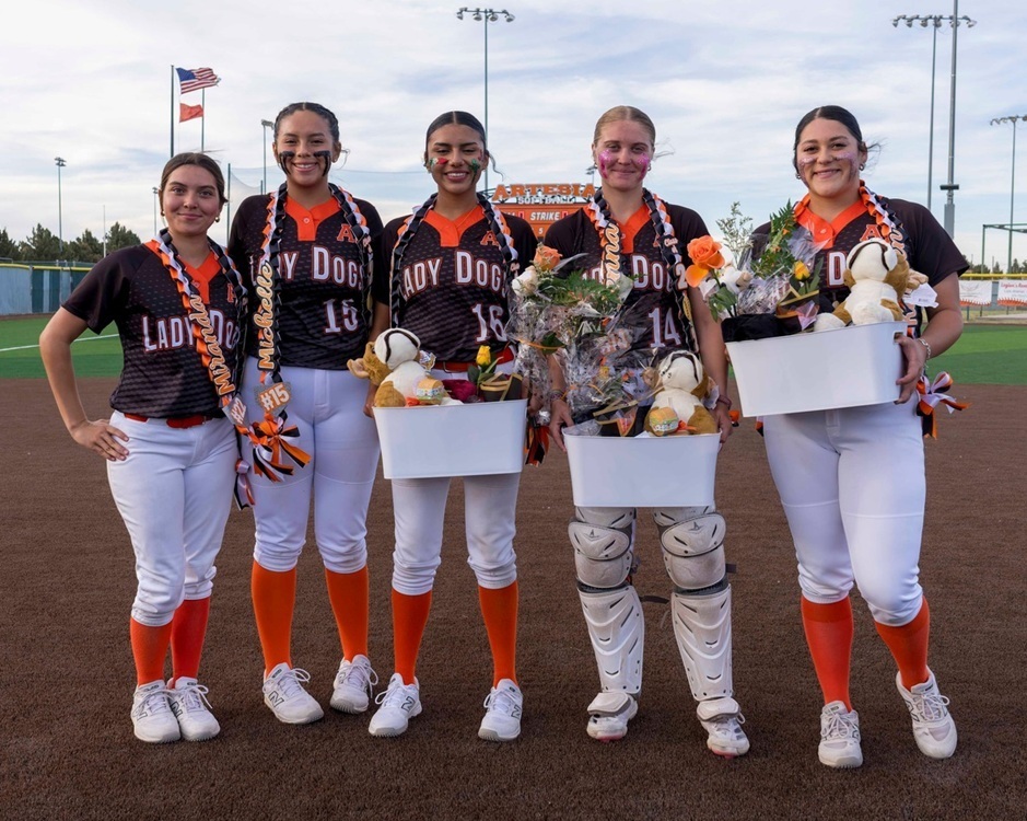 Five teen girls in black, orange and white softball uniforms smile for the camera. Some hold gift baskets.