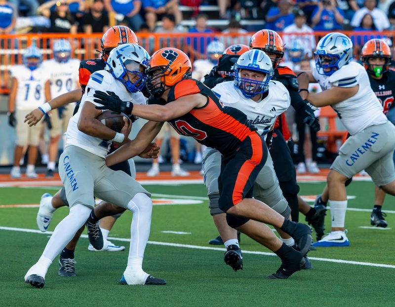 A teen boy in a black and orange football uniform tackles a ball carrier in silver and blue.