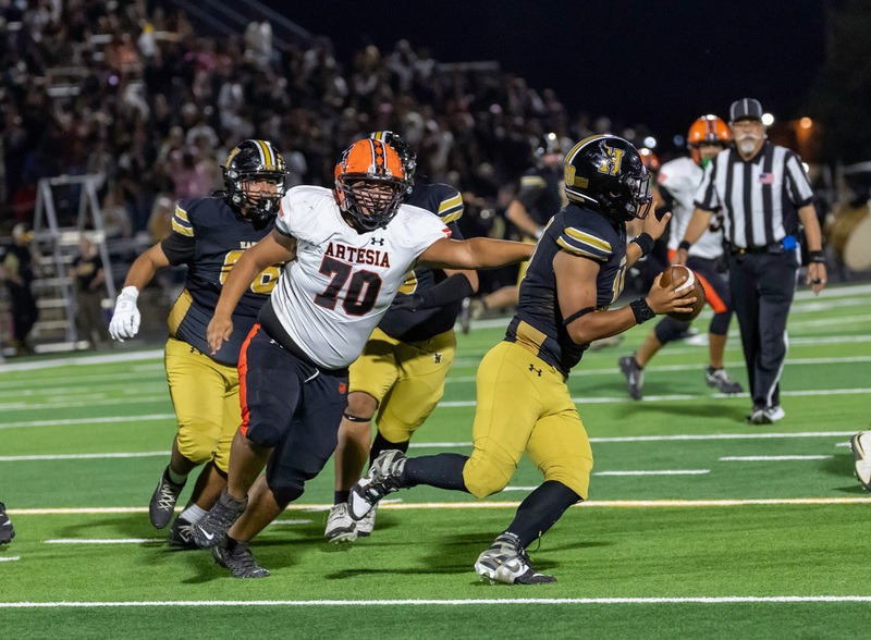 A teen boy in an orange, black and white football uniform chases down an opposing quarterback in black and gold.