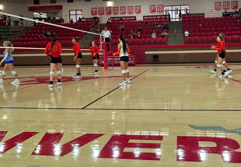A high school volleyball team in orange and black stands on their half of a court.